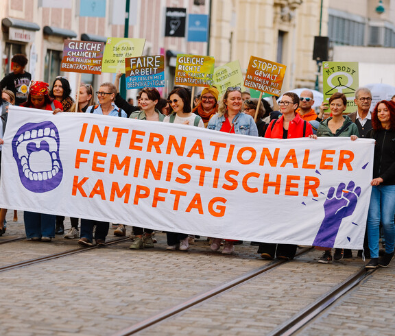 Eine Gruppe von Frauen und an ein paar Männer bildet die Spitze des Demonstrationszugs am Weltfrauentag 2026 in Linz. Sie hält ein Banner in Händen, auf dem steht: Internationaler Feministischer Kampftag.