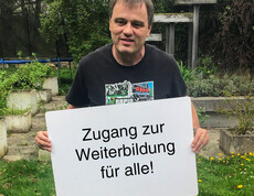Ein Mann hält ein Schild in der Hand auf dem steht "Zugang zur Weiterbildung für alle"