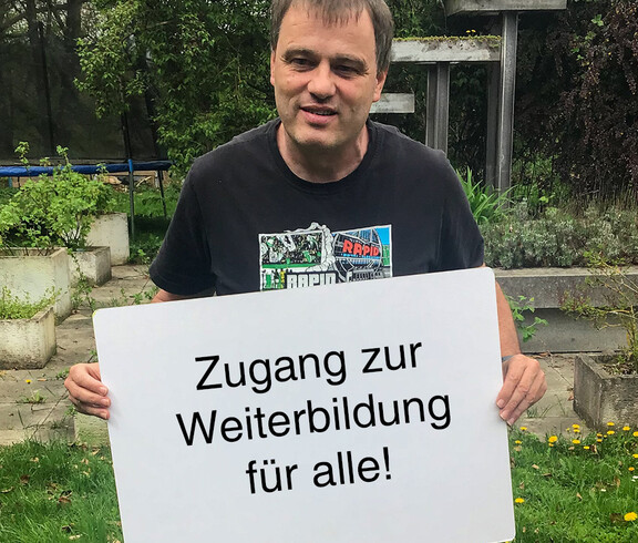 Ein Mann hält ein Schild in der Hand auf dem steht "Zugang zur Weiterbildung für alle"