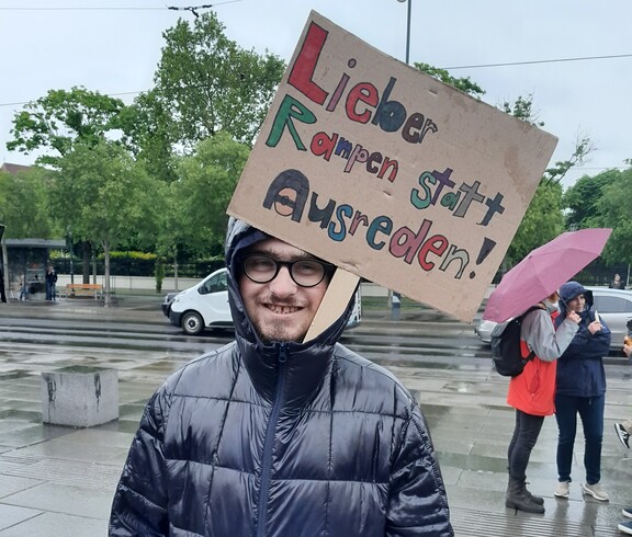Ein junger Mann mit einem Schild bei der Baustelle Inklusion vor dem Parlament in Wien 2025.