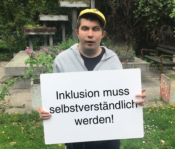 Ein Mann hält ein Schild in der Hand auf dem steht "Inklusioin muss selbstverständlich werden"