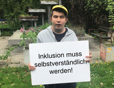 Ein Mann hält ein Schild in der Hand auf dem steht "Inklusioin muss selbstverständlich werden"