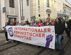 Demonstrationszug beim Feministischen Kampftag 2026 mit einem großen Banner im Vordergrund. Im Hintergrund Häuser auf der Linzer Landstraße.