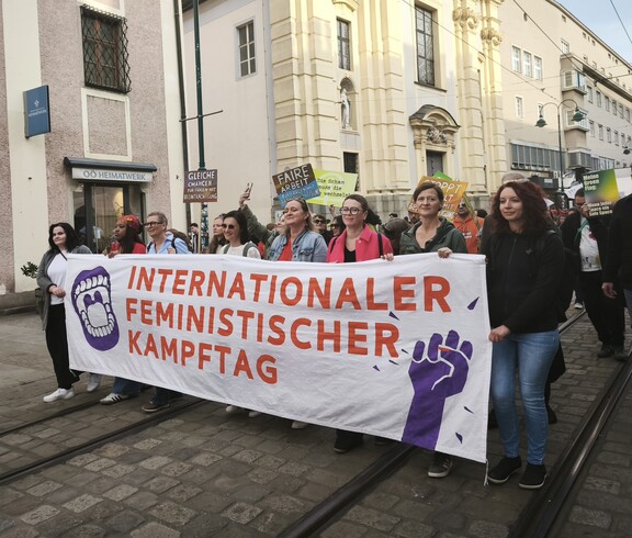 Demonstrationszug beim Feministischen Kampftag 2026 mit einem großen Banner im Vordergrund. Im Hintergrund Häuser auf der Linzer Landstraße.