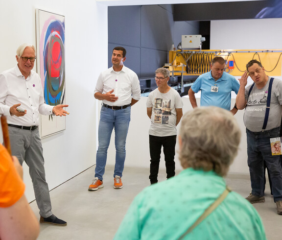 Ein Mann spricht vor einer Gruppe von Besuchern in einem Ausstellungsraum mit zeitgenössischer Kunst.