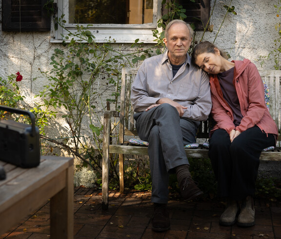 Frau lehnt an der Schulter ihres Mannes, sie sitzen im Garten 