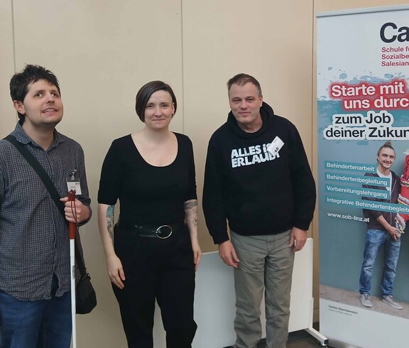 Drei Personen vor einem Plakat