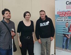 Drei Personen vor einem Plakat