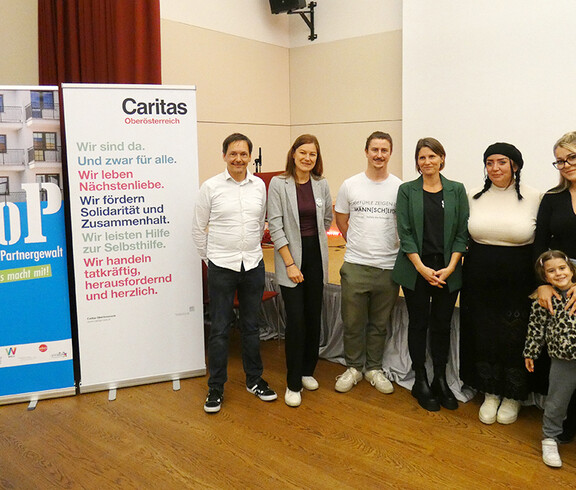 Teilnehmer*innen der Filmvorführung "Ein Tag ohne Frauen" 2025 in Wels neben Roll ups von STOP und Caritas OÖ