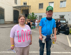 Eine Frau in einem rosa Shirt und ein Mann in einem blauem Shirt stehen vor einem Gebäude. 