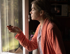 Frau steht vor offenem Fenster und hat kleinen Käfer in der Hand