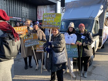 Mehrere Frauen halten ein Plakat in der Hand und blicken in die Kamera. 