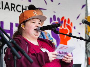 Eine junge Frau mit Kappe hält auf einer Bühne zum Weltfrauentag eine Rede