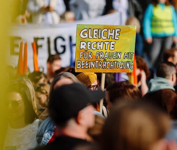 Ein Schild, auf dem "Gleiche Rechte für Frauen mit Beeinträchtigungen" steht, wird bei einer Demonstration in die Höhe gehalten