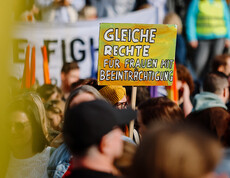 Ein Schild, auf dem "Gleiche Rechte für Frauen mit Beeinträchtigungen" steht, wird bei einer Demonstration in die Höhe gehalten