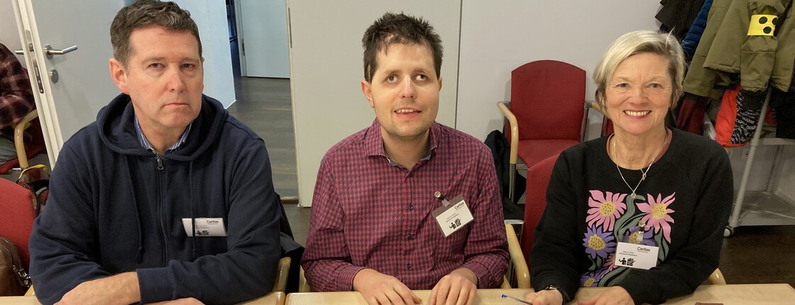 Zwei Männer und eine Frau sitzen an Tischen bei einer Pressekonferenz