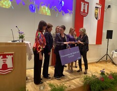 Mehrer Frauen stehen auf einer Bühne und halten einen Karton mit der Gewinnsumme in der Hand. 