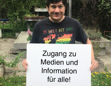 Ein Mann hält ein Schild in der Hand auf dem steht "Zugang zu Medien und Information für alle"