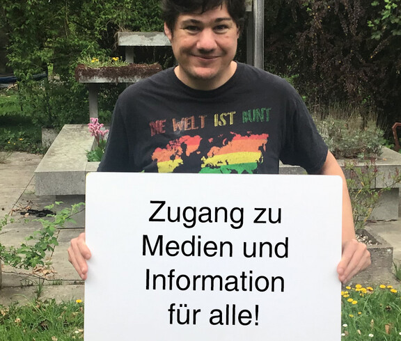 Ein Mann hält ein Schild in der Hand auf dem steht "Zugang zu Medien und Information für alle"