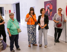Eine Gruppe von Frauen steht in einem Ausstellungsraum für zeitgenössische Kunst. Eine der Frauen hat einen Stock.