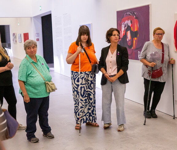 Eine Gruppe von Frauen steht in einem Ausstellungsraum für zeitgenössische Kunst. Eine der Frauen hat einen Stock.