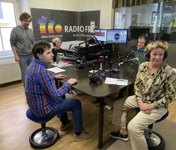 Drei Personen sitzen in einem Aufnahmestudio. 