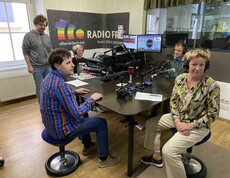 Drei Personen sitzen in einem Aufnahmestudio. 