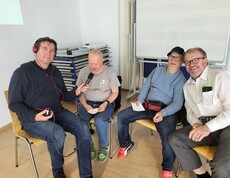 Drei Personen sitzen auf Stühlen und blicken in die Kamera. 