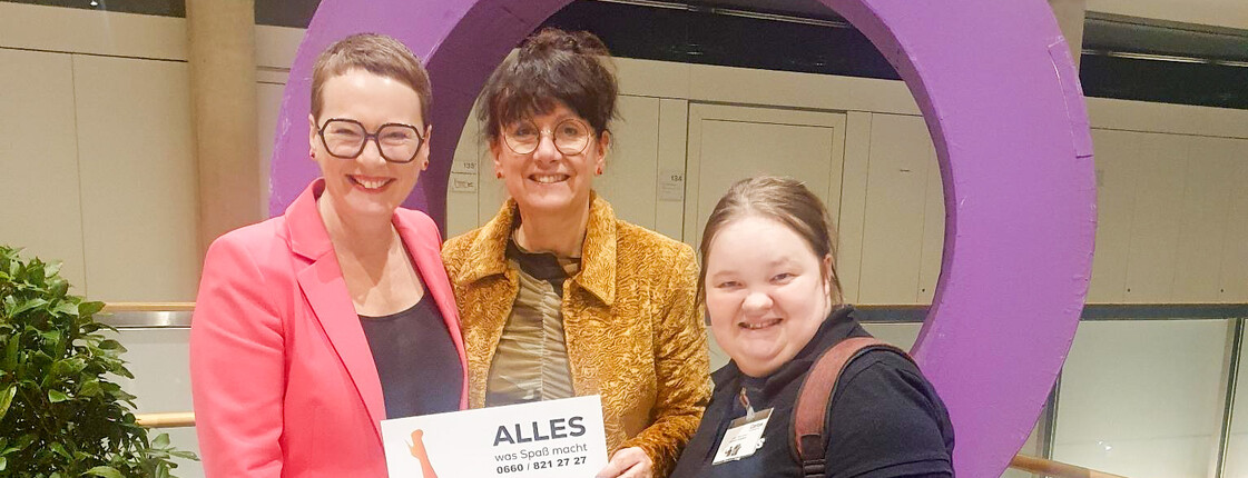 3 Frauen stehen vor einem großen violetten Frauensymbol bei der Frauenpreisverleihung der Stadt Linz 2026