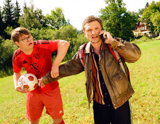 Szenerie: Bursch hält Fußball, Mann telefoniert und hält Bursch fest 