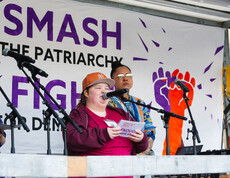 Eine junge Frau mit Kappe hält auf einer Bühne zum Weltfrauentag eine Rede