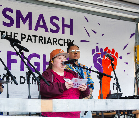 Eine junge Frau mit Kappe hält auf einer Bühne zum Weltfrauentag eine Rede