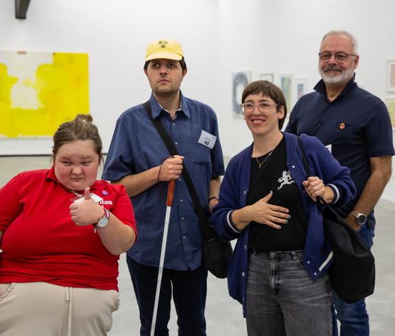 Eine Gruppe von zwei Frauen und zwei Männern in einem Ausstellungsraum mit zeitgenössischer Kunst. Einer der Männer hält einen Blindenstock.