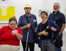 Eine Gruppe von zwei Frauen und zwei Männern in einem Ausstellungsraum mit zeitgenössischer Kunst. Einer der Männer hält einen Blindenstock.