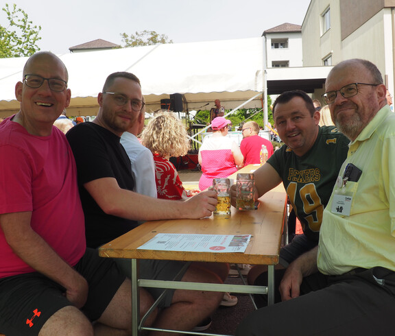 Vier Männer sitzen unter einem Sonnenschirm auf einem Biertisch