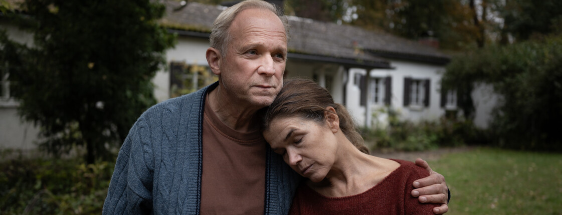 Frau lehnt sich im Garten an die Schulter ihres Mannes 