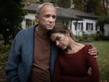 Frau lehnt sich im Garten an die Schulter ihres Mannes 