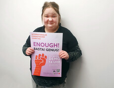 Eine Frau steht vor einer weißen Wand und hält ein Plakat in die Kamera.