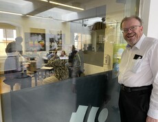 Ein Mann steht vor einem Galsfenster vor dem Radioaufnahmestudio und schaut in die Kamera.