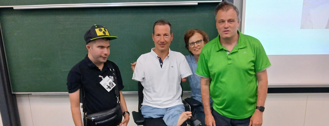 Szene in Hörsaal: Vier Personen, Mann in Spezial-Rollstuhl