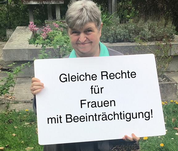 Ein Frau hält ein Schild in der Hand auf dem steht "Gleiche Rechte für Frauen mit Beeinträchtigung"