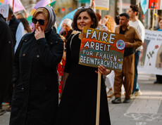Zwei Frauen gehen bei der Demonstration am Weltfrauentag 2026 mit einem Schild mit. Auf dem Schild steht "Faire Arbeit für Frauen mit Beeinträchtigung"
