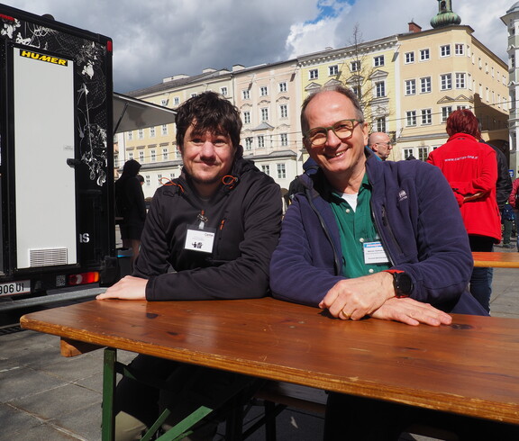 Zwei Personen sitzen auf einem Tisch auf einem öffentlichen Platz. 