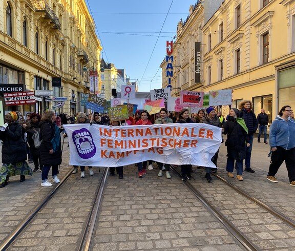 Viele Personen halten ein Plakat in der Hand und gehen eine Straße entlang. 