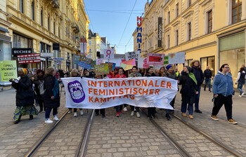 Viele Personen halten ein Plakat in der Hand und gehen eine Straße entlang. 