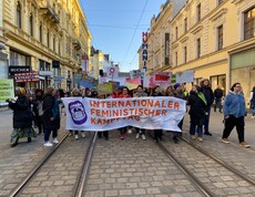 Viele Personen halten ein Plakat in der Hand und gehen eine Straße entlang. 