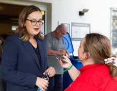Eine junge Frau mit Brille wird von einer anderen jungen Frau mit einem Handy interviewt.