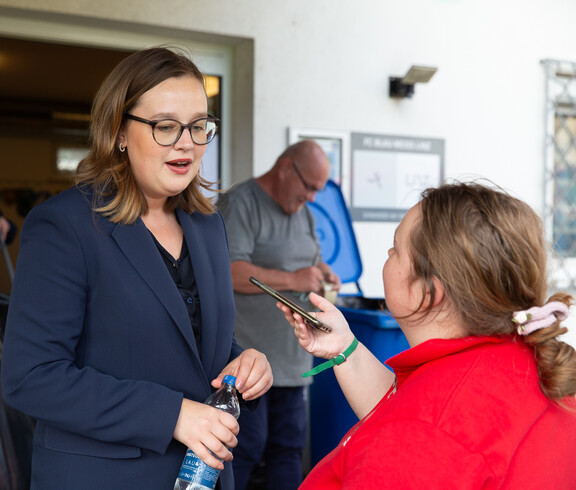 Eine junge Frau mit Brille wird von einer anderen jungen Frau mit einem Handy interviewt.
