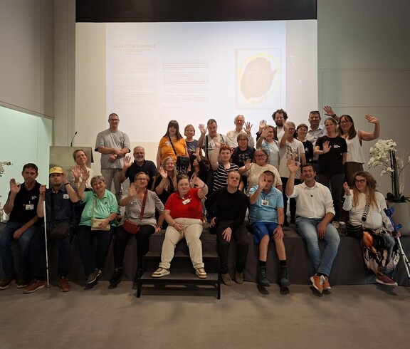 Eine Gruppe von Menschen sitzt für ein Gruppenbild posierend vor einer Leinwand