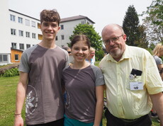 Zwei Jugendliche und ein Mann stehen vor einem Gebäude im Freien und lachen in die Kamera